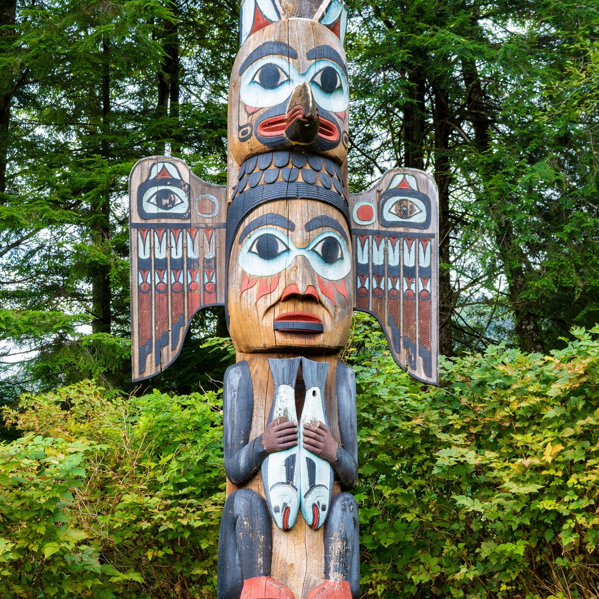 A peaceful view of Totem Bight State Park with logs on the shore, rocky coastline and a forested backdrop leading to the distant waters.