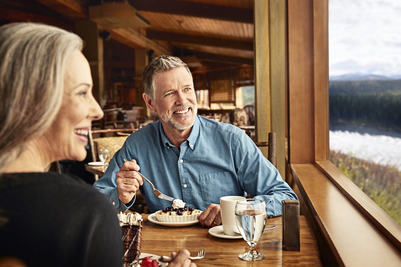 A smiling older couple enjoying dessert together at a rustic restaurant aboard a Princess Cruises ship.