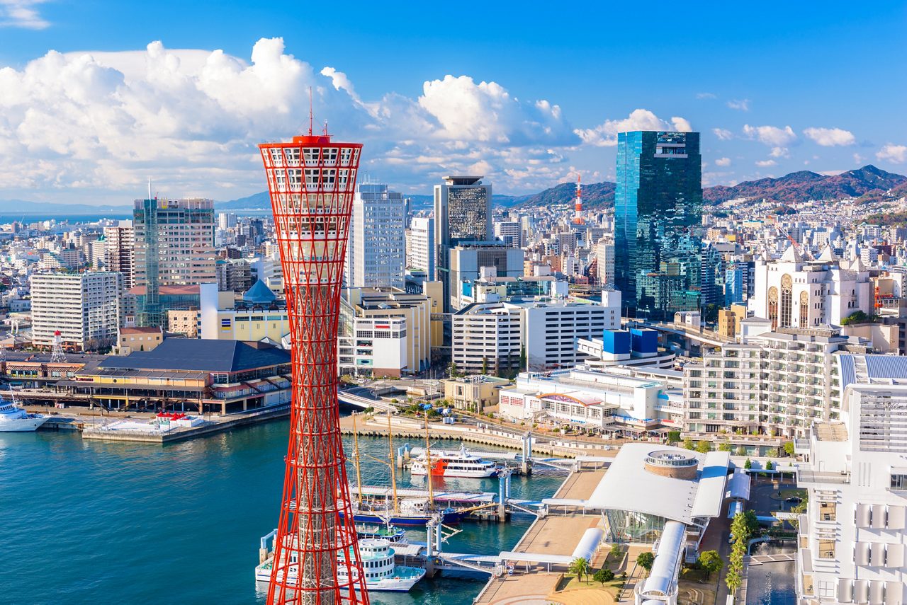 Aerial view of Kobe, Japan featuring the red Port Tower, modern buildings and harbor with docked boats.