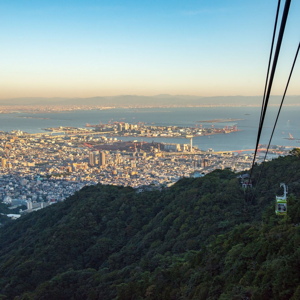 Aerial view from Mt. Rokko showing a cable car descending toward Kobe city with Osaka Bay in the background.