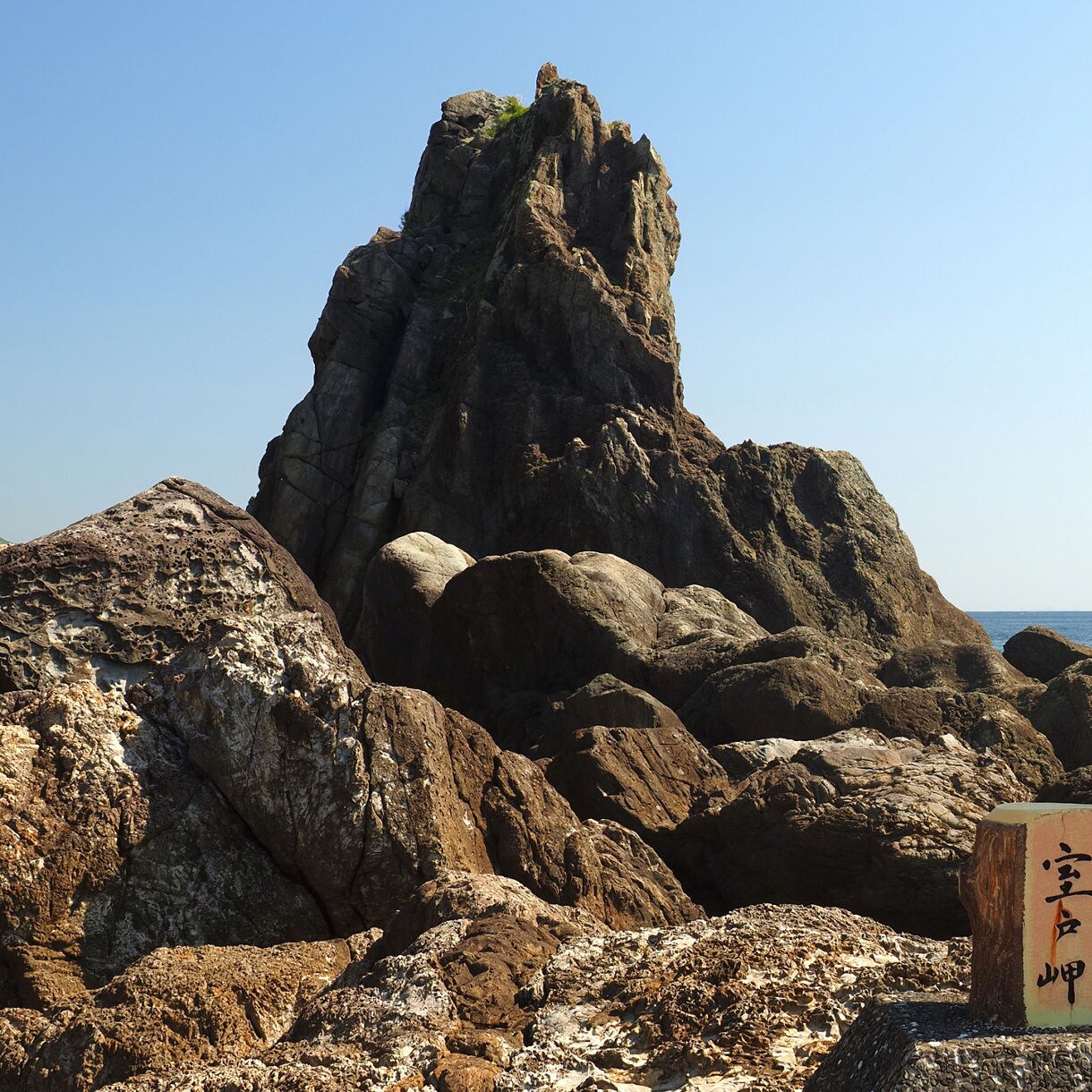 Rocky coastline at Cape Muroto with large sea cliffs, weathered boulders and wooden signposts by the ocean.