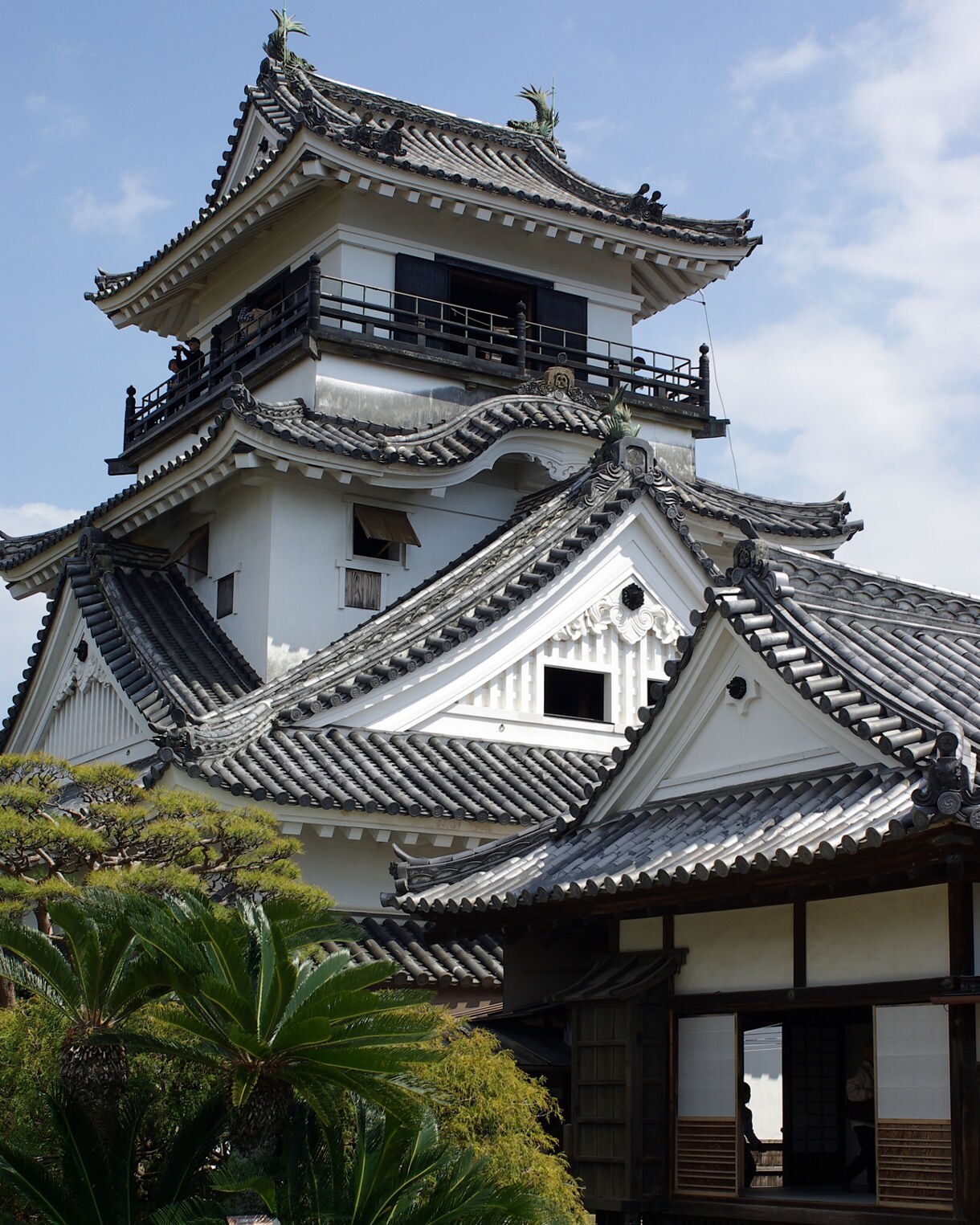Traditional white Japanese castle with tiled roofs and curved gables, surrounded by manicured plants and trees.