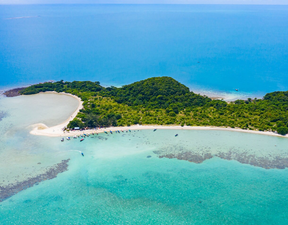 Aerial view of Koh Madsum showing lush greenery, white sandy beaches and boats anchored in clear turquoise waters.