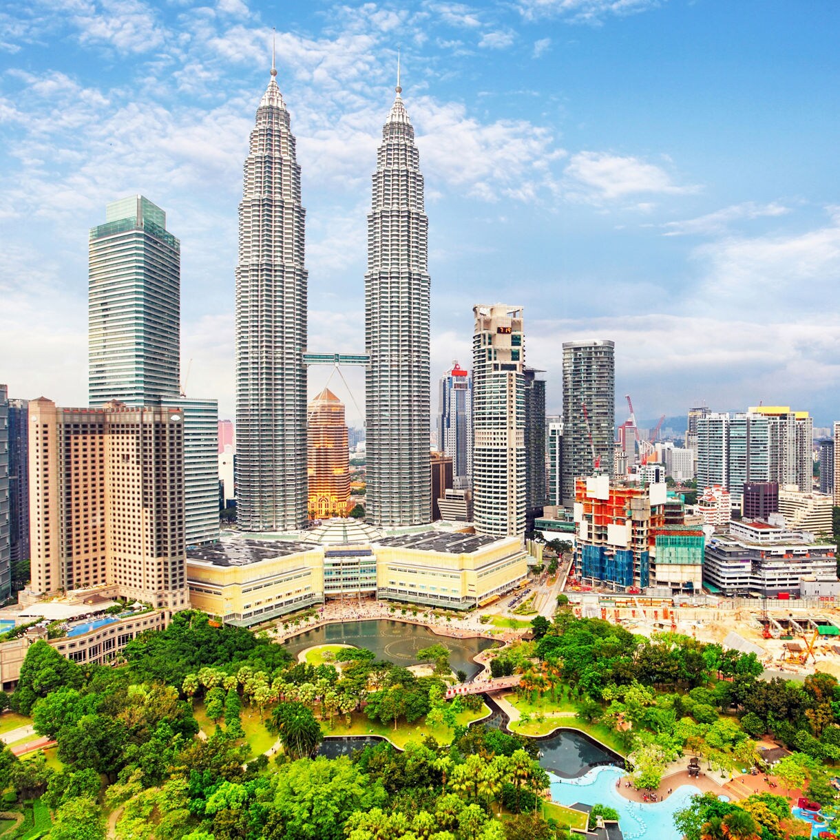 Aerial view of Kuala Lumpur with the Petronas Twin Towers rising above modern skyscrapers and a city park.