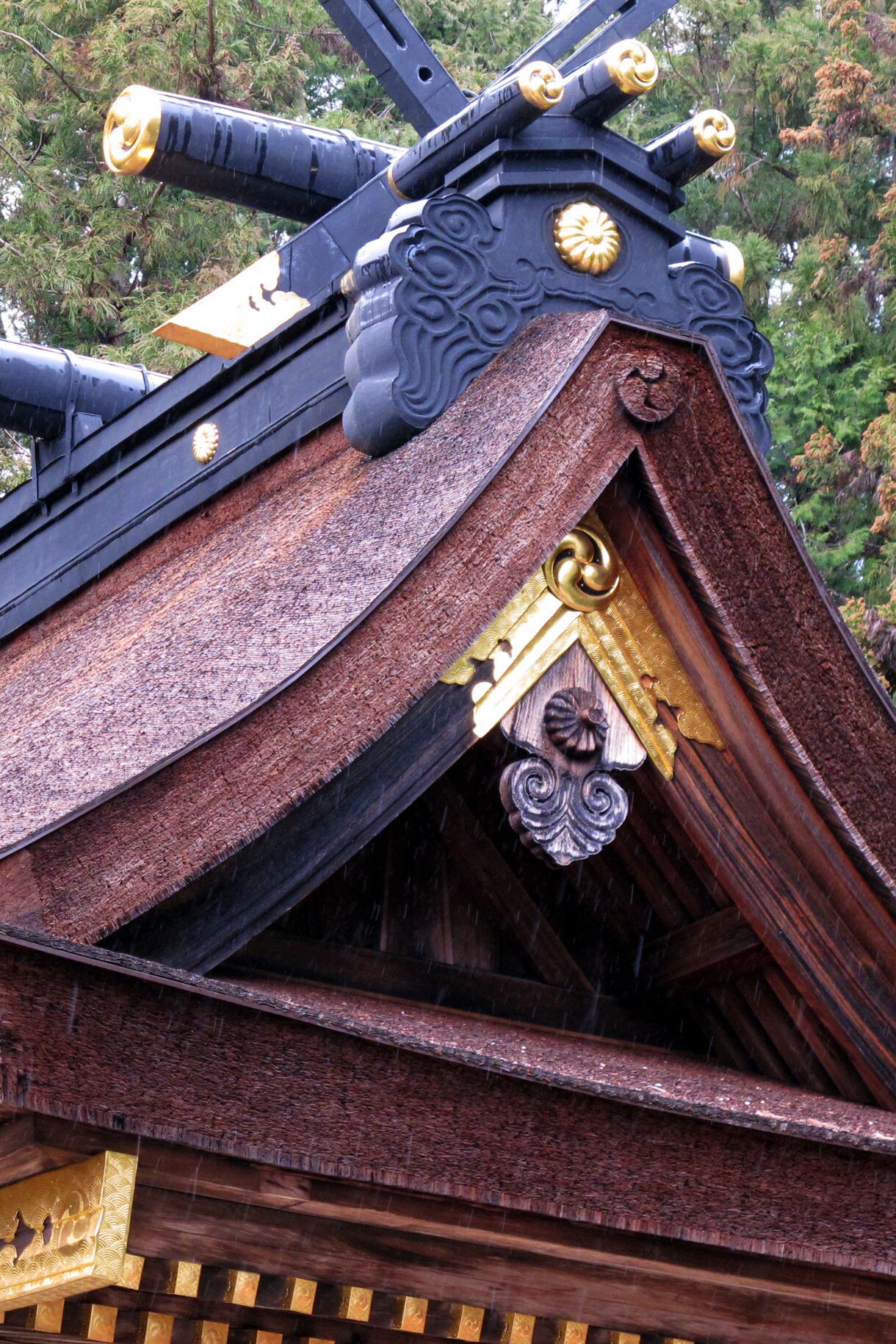 Close-up view of traditional Japanese temple roof architecture featuring curved clay tiles, ornate wooden brackets, and decorative elements typical of Kumano shrine construction.