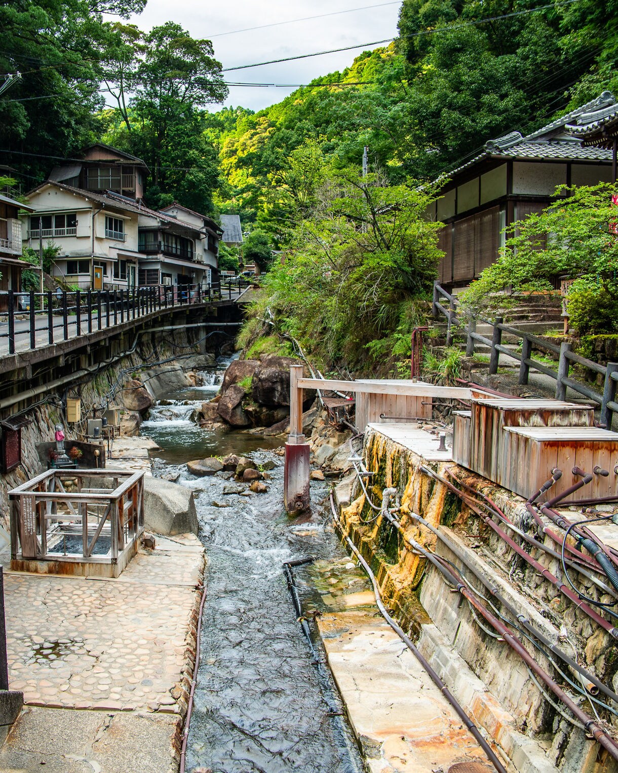 A narrow stream runs through Yunomine Onsen, lined with old wooden bathhouses, colorful pipes and traditional homes nestled in forested hills.