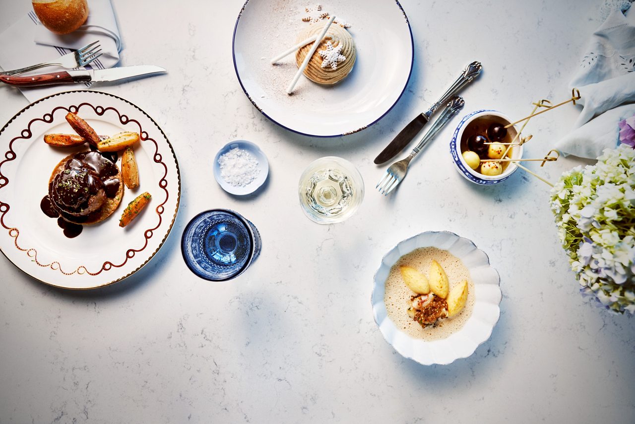 An overhead view of an elegantly plated dessert and appetizer spread on a table with fine china and fresh flowers.
