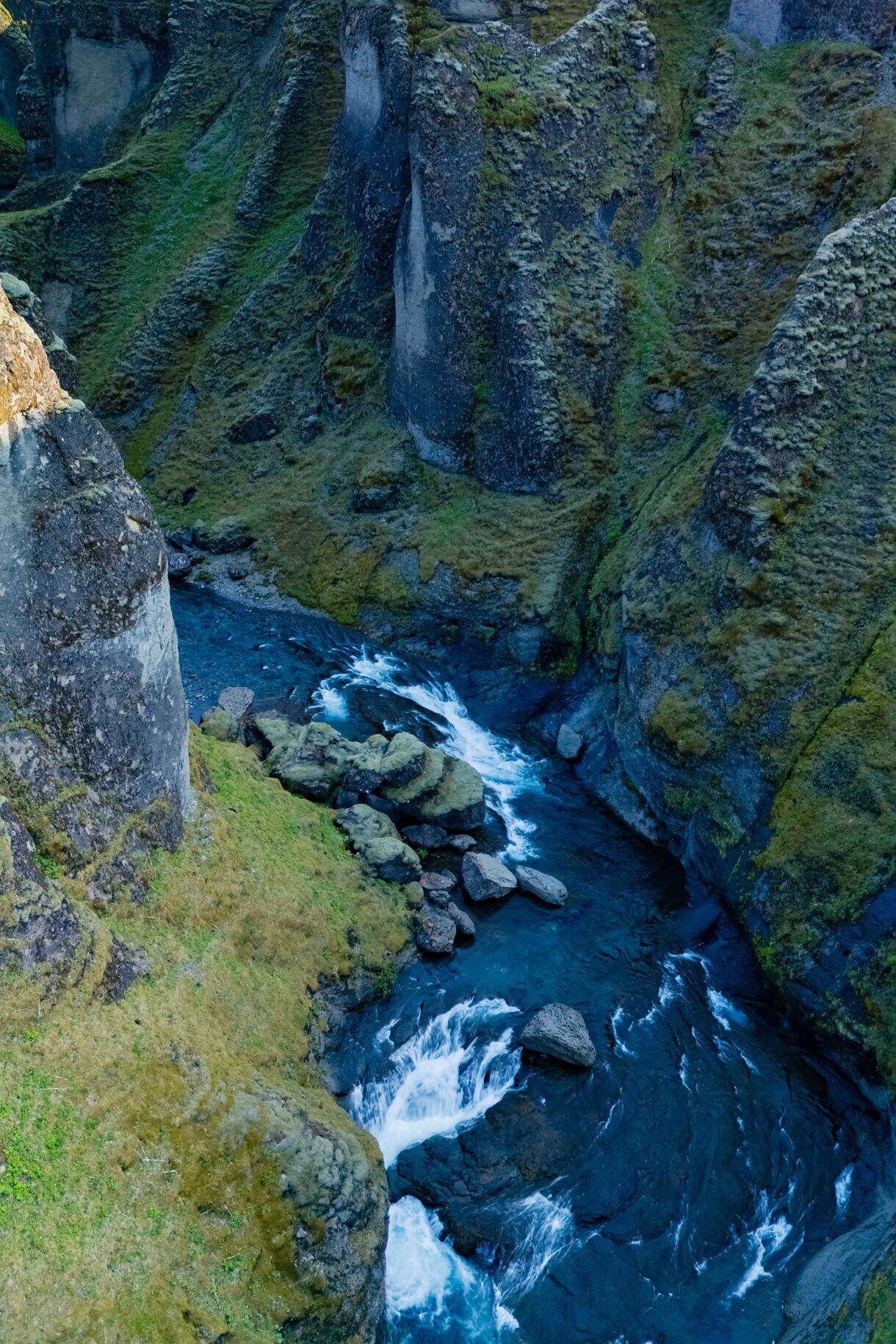 Narrow river with whitewater flowing between tall mossy canyon walls under soft daylight.