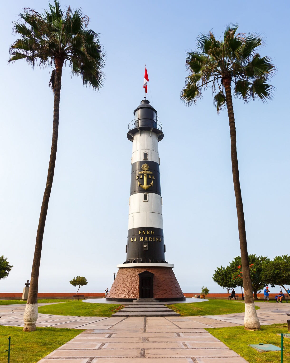 A tall black and white lighthouse in Miraflores, Peru framed by two palm trees with a clear blue sky overhead.