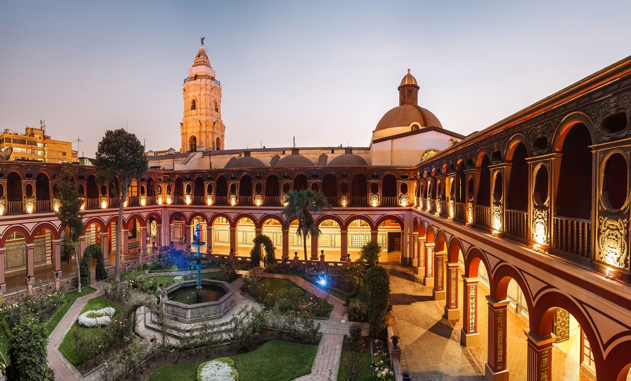 Exterior view of the Santo Domingo Convent in Lima, Peru, highlighting its historic architecture with a mix of colonial and baroque styles. The building features a prominent bell tower and intricate details on its facade, set against a clear blue sky.