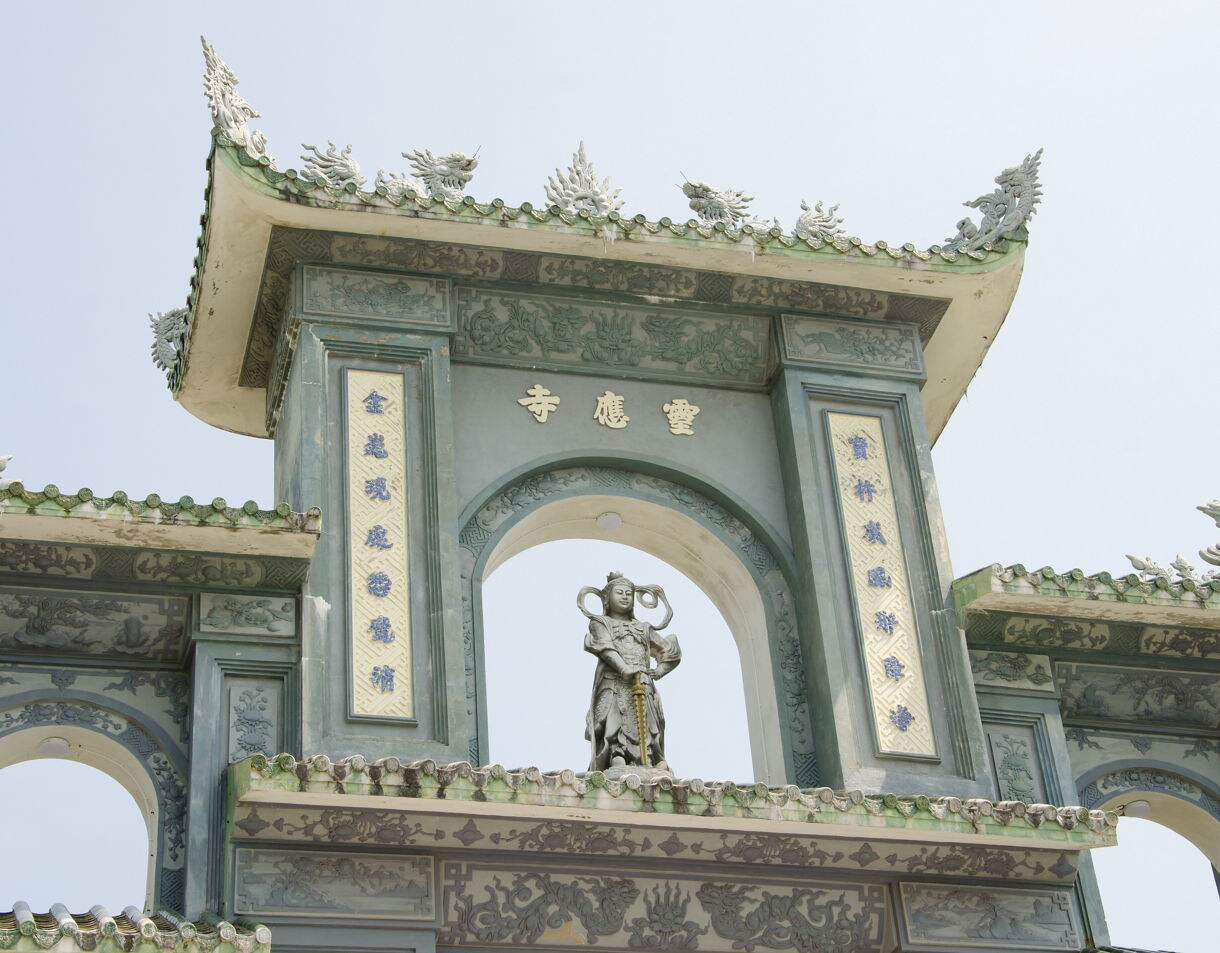 Detailed view of Linh Ứng Pagoda’s ornate gateway in Da Nang, Vietnam, featuring green-tiled roofs, dragon motifs and a central statue of a guardian deity.