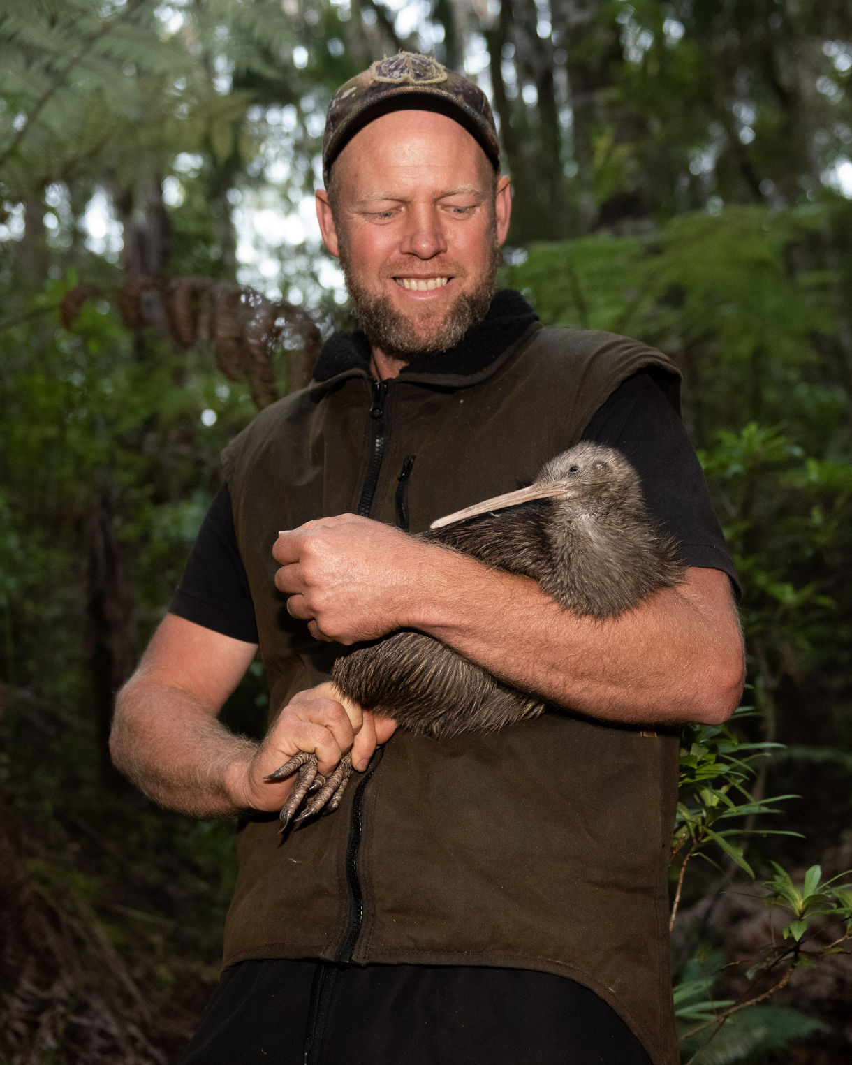 Bay Bush Action group leader smiles standing in Opua State Forest while gently holding a kiwi bird in his arms.