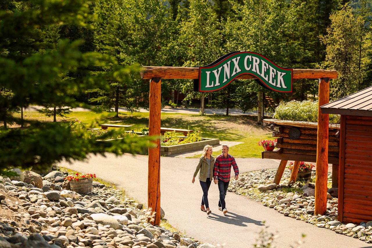 Couple walking under Lynx Creek entrance sign outdoors.