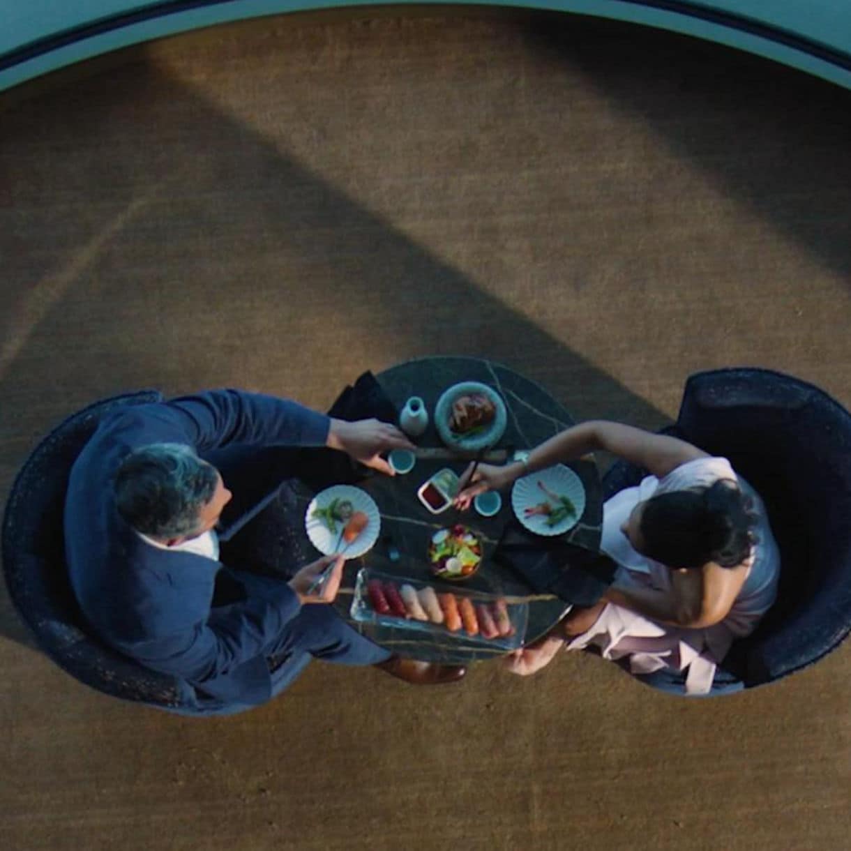 Overhead view of two people dining at a circular table, sharing food and drinks in an intimate restaurant setting.