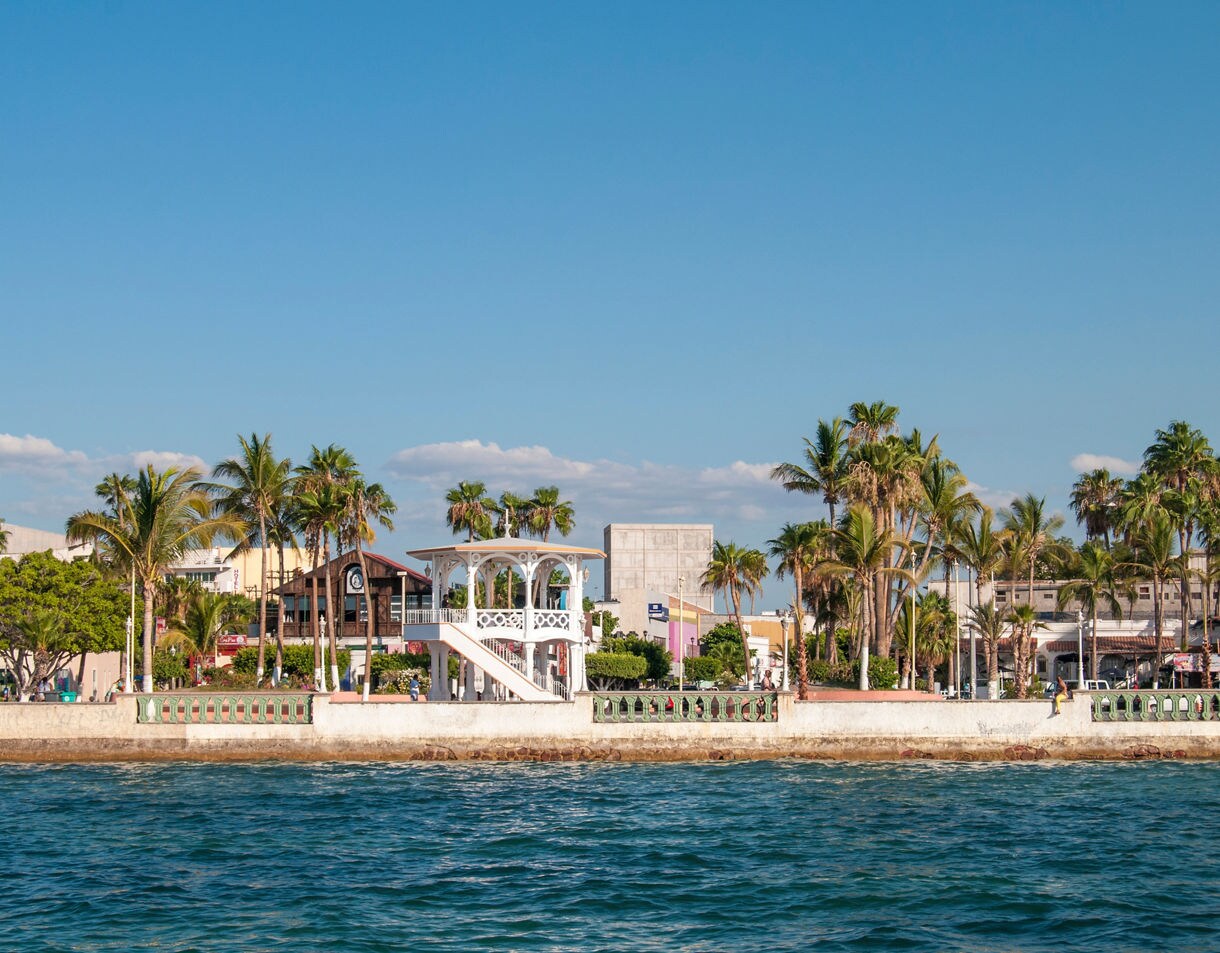 Waterfront promenade of La Paz, Mexico featuring palm trees, a white gazebo and colorful buildings by the sea.