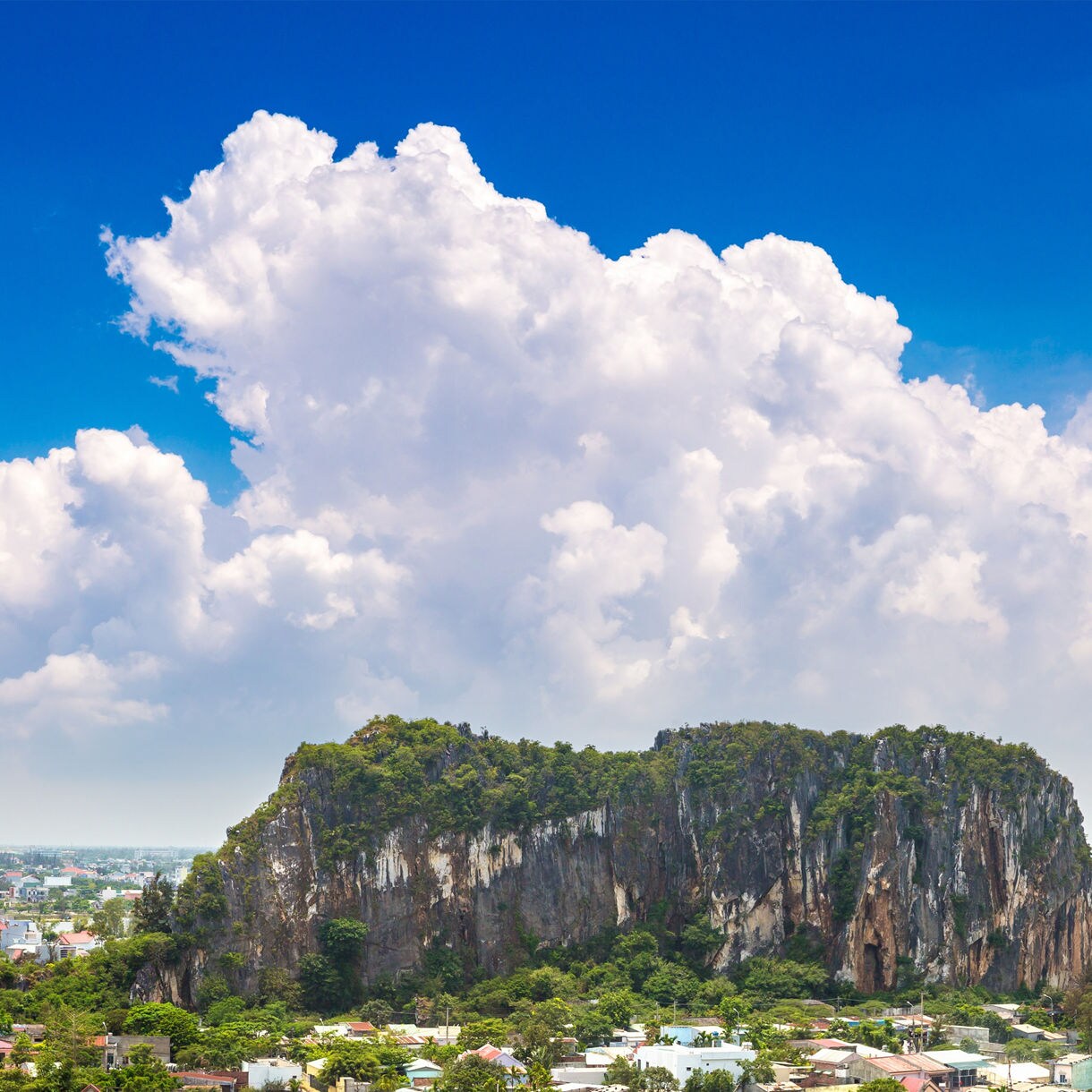 Panoramic view of Da Nang’s Marble Mountains, featuring green limestone hills surrounded by city buildings under a vivid blue sky with billowing clouds.