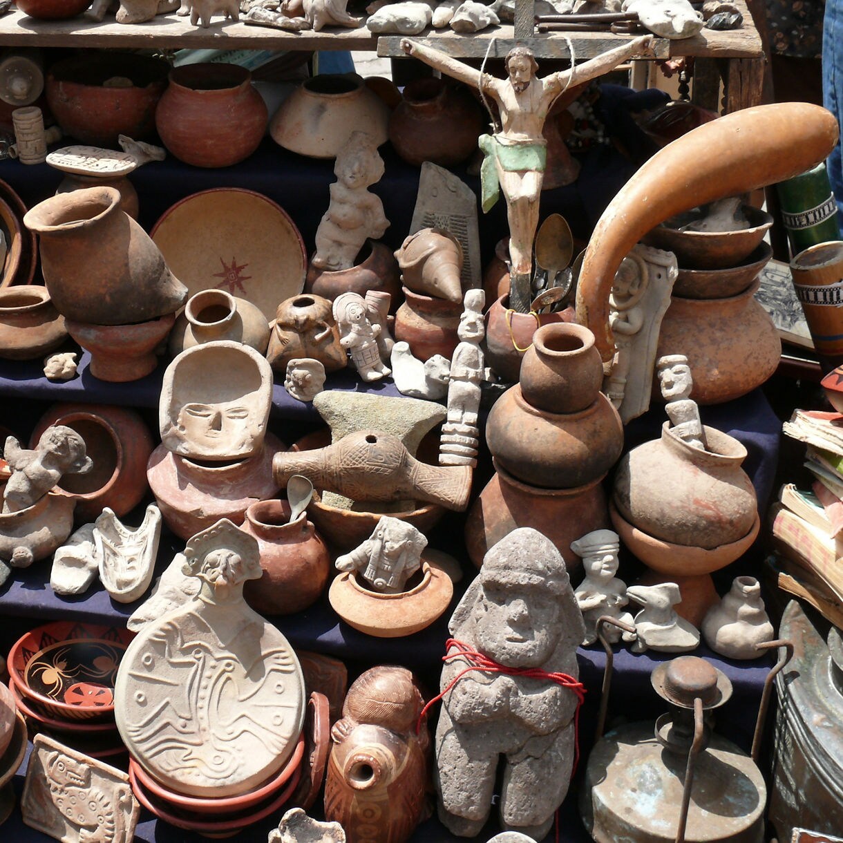 Assortment of clay pots, carved figurines, masks and rustic artifacts arranged tightly on a crowded market display.