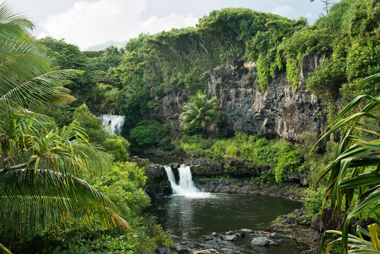 A tranquil view of the waterfalls at Ohe'o Gulch, or the Seven Sacred Pools, in Maui, Hawaii, with waterfalls flowing into natural pools framed by lush tropical vegetation and towering cliffs in Haleakalā National Park.