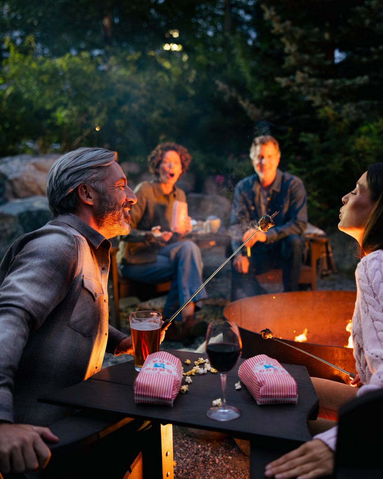 Moose grazing in wetland grasses along waterfront with Anchorage city skyline and misty mountain ranges visible across the water under cloudy skies.