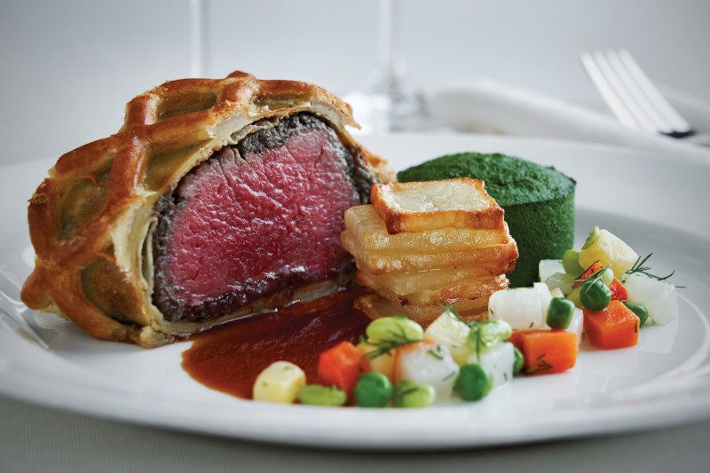 Beef wellington with colorful vegetable medley and green puree.