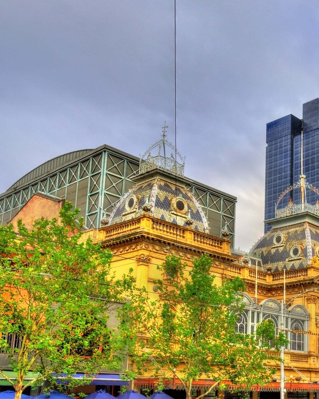 The ornate golden facade of Melbourne’s Princess Theatre surrounded by modern skyscrapers and leafy trees under a partly cloudy sky.