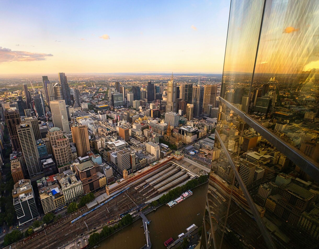 Aerial view of Melbourne’s skyline at sunset with golden reflections on a skyscraper window and the Yarra River below.