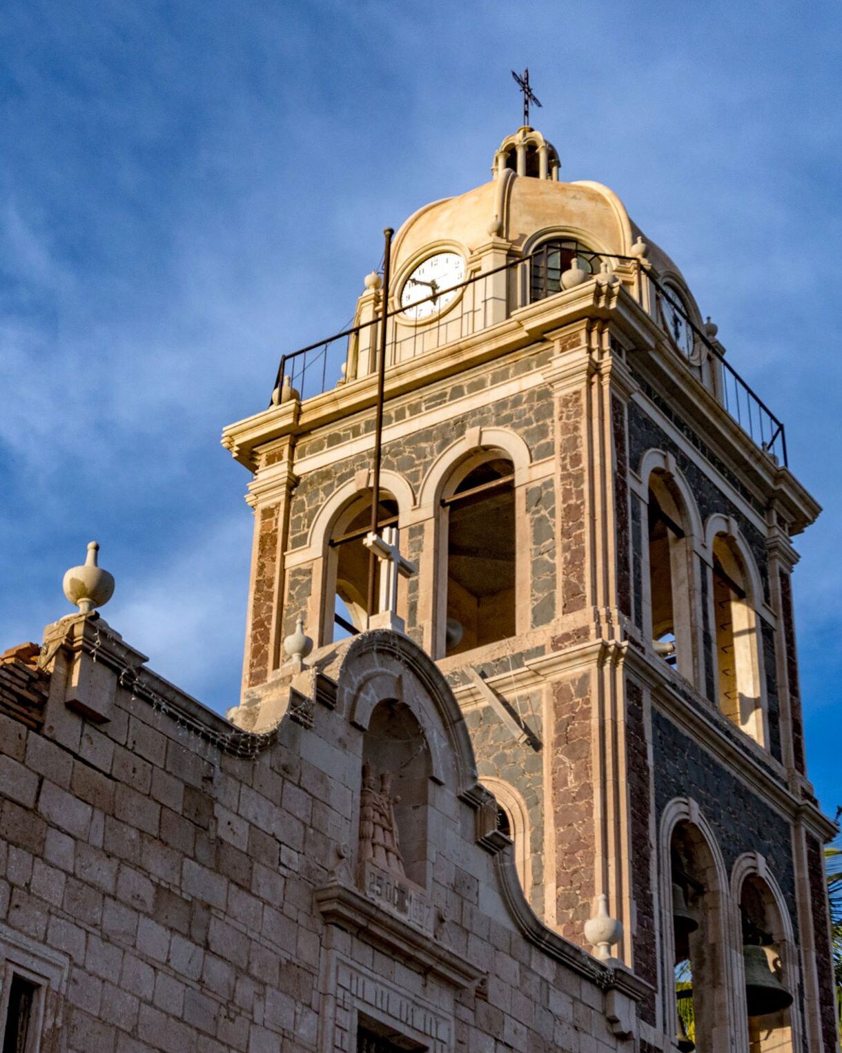 Bell tower of the Mission of Our Lady of Loreto in Loreto, Mexico, against a blue sky, showcasing its colonial architecture.