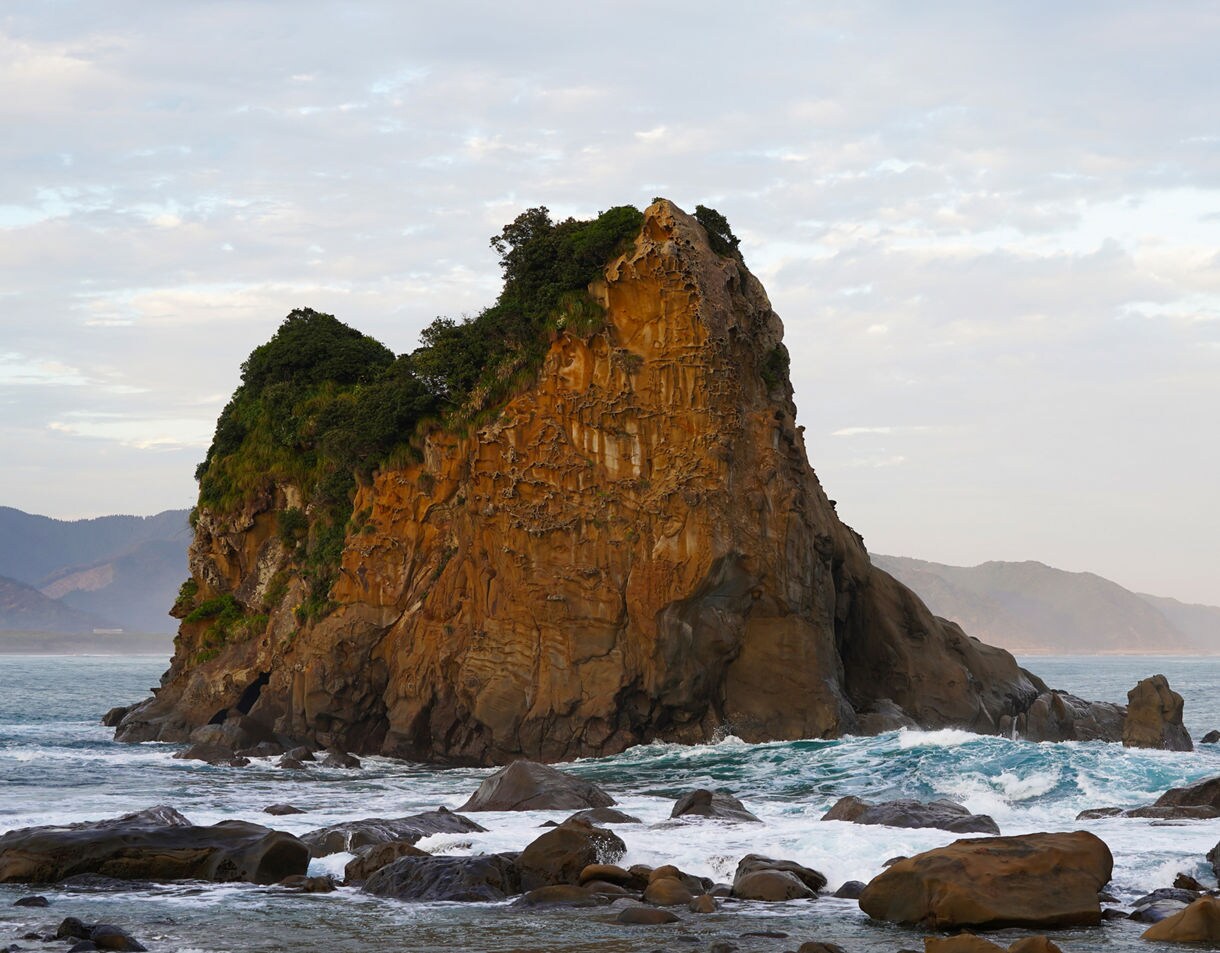 Large volcanic sea cliff rising from the ocean in Miyazaki, Japan, with waves crashing against rocky shores.
