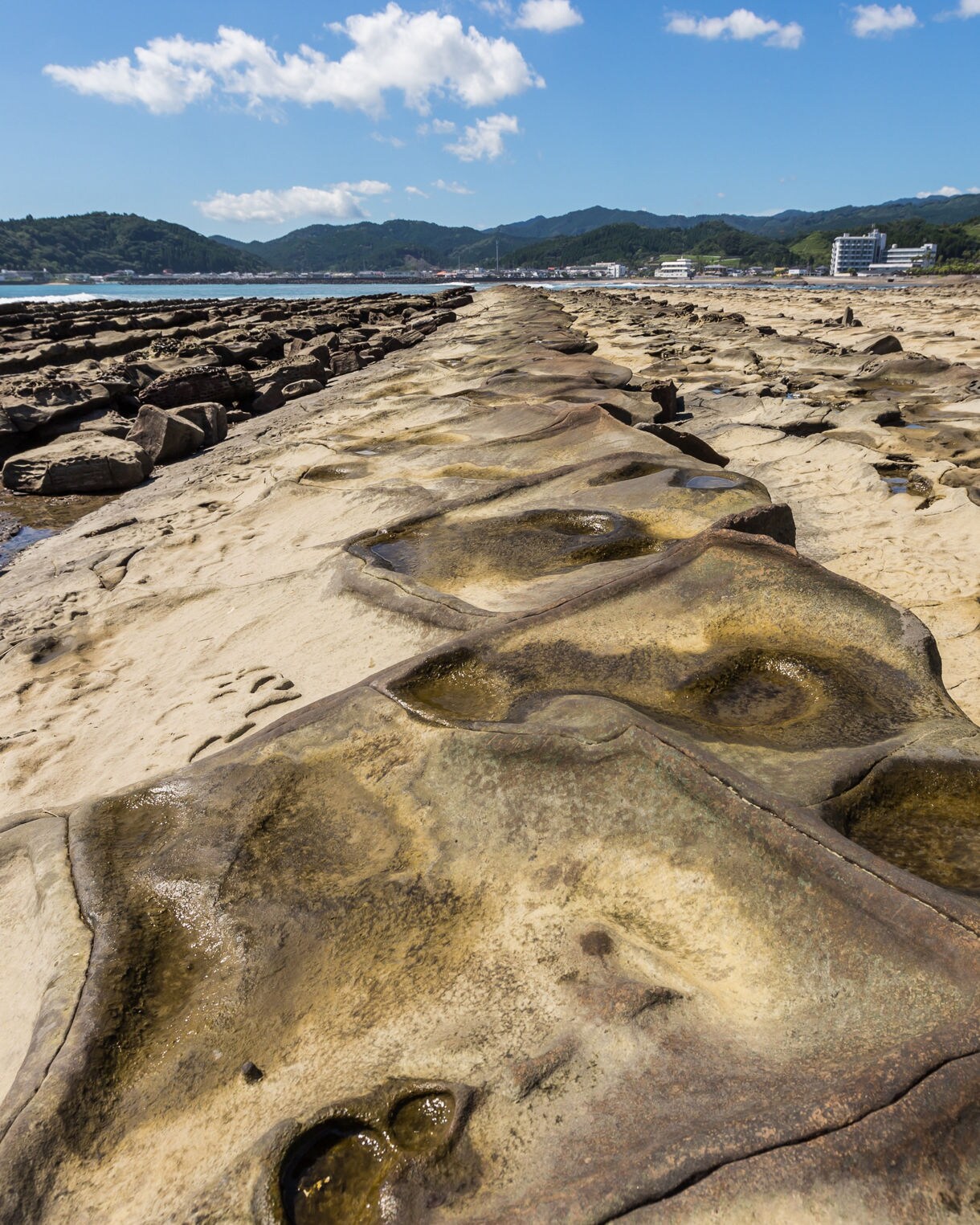 Rocky coastal formations known as the Devil’s Washboard in Miyazaki, Japan, with flat, ridged stone surfaces and tide pools under a bright sky.
