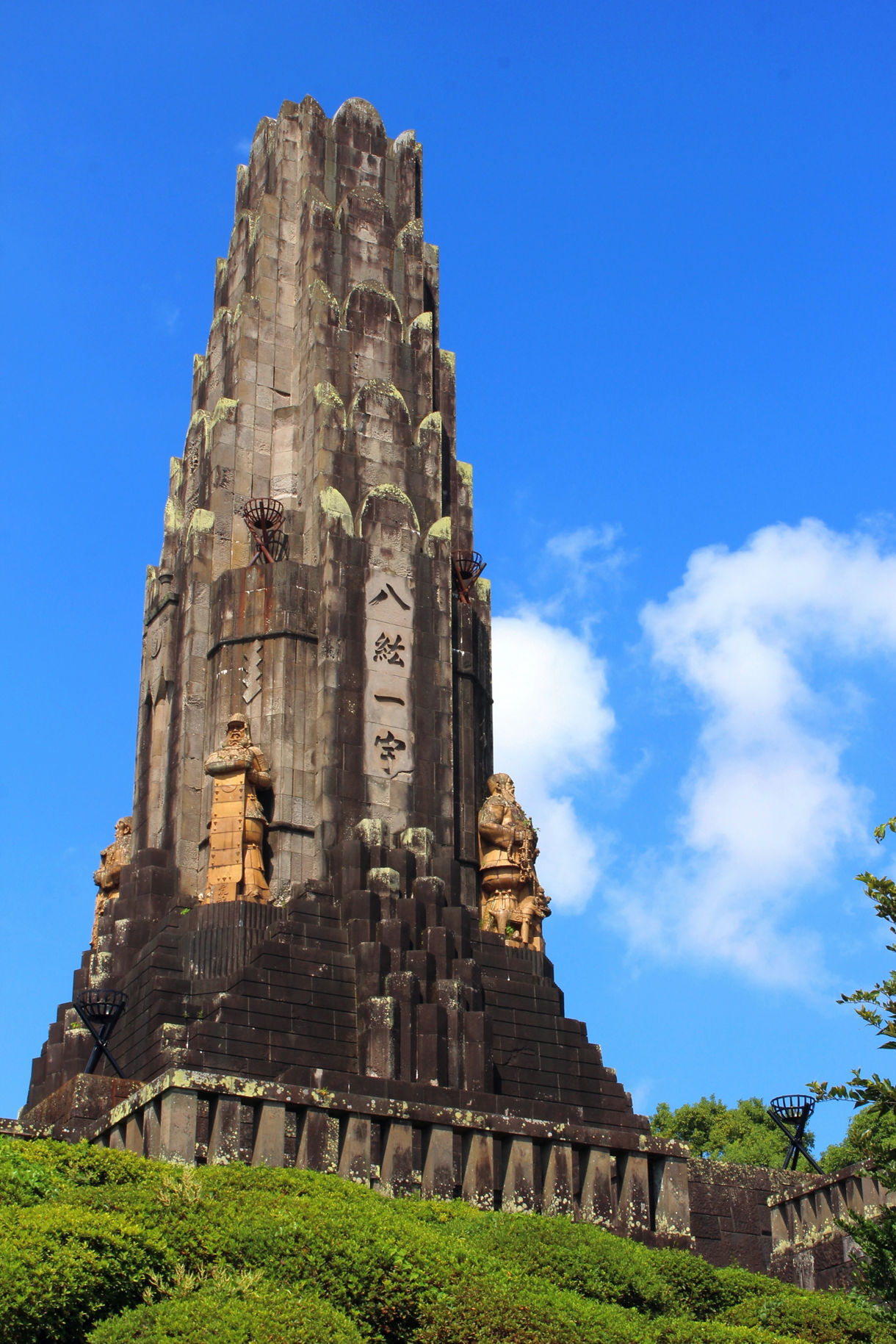 Heiwadai Peace Tower featuring dark stone architecture, carved figures, and Japanese characters against a clear sky.