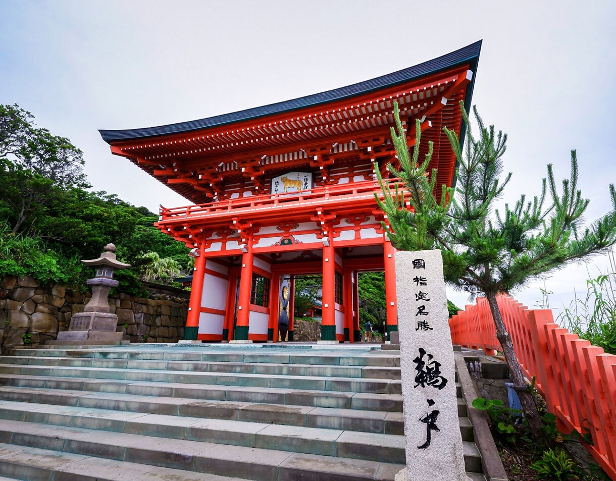 Bright red torii-style gate at Udo Shrine in Miyazaki, Japan, with stone steps, greenery, and traditional architectural details.