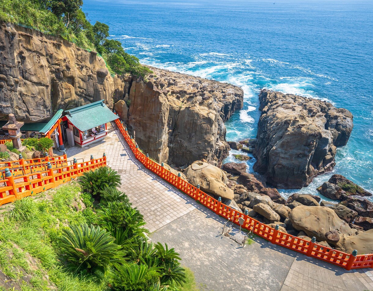 A bright red walkway leading to a grotto-style shrine built into seaside cliffs overlooking the Pacific Ocean.