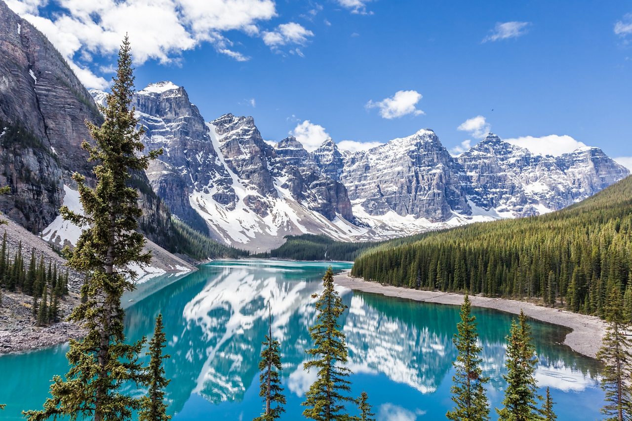 A breathtaking view of Moraine Lake in Banff National Park, Canada, with crystal-clear turquoise waters reflecting the towering snow-capped peaks of the Canadian Rockies, surrounded by dense pine forests.