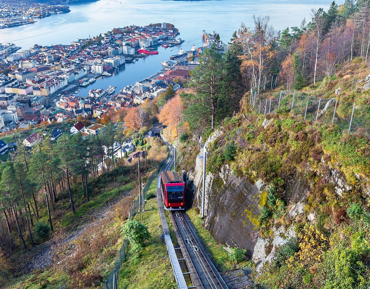 Red Fløibanen funicular climbing Mount Fløyen with panoramic view of Bergen city, harbor and cruise ships below.
