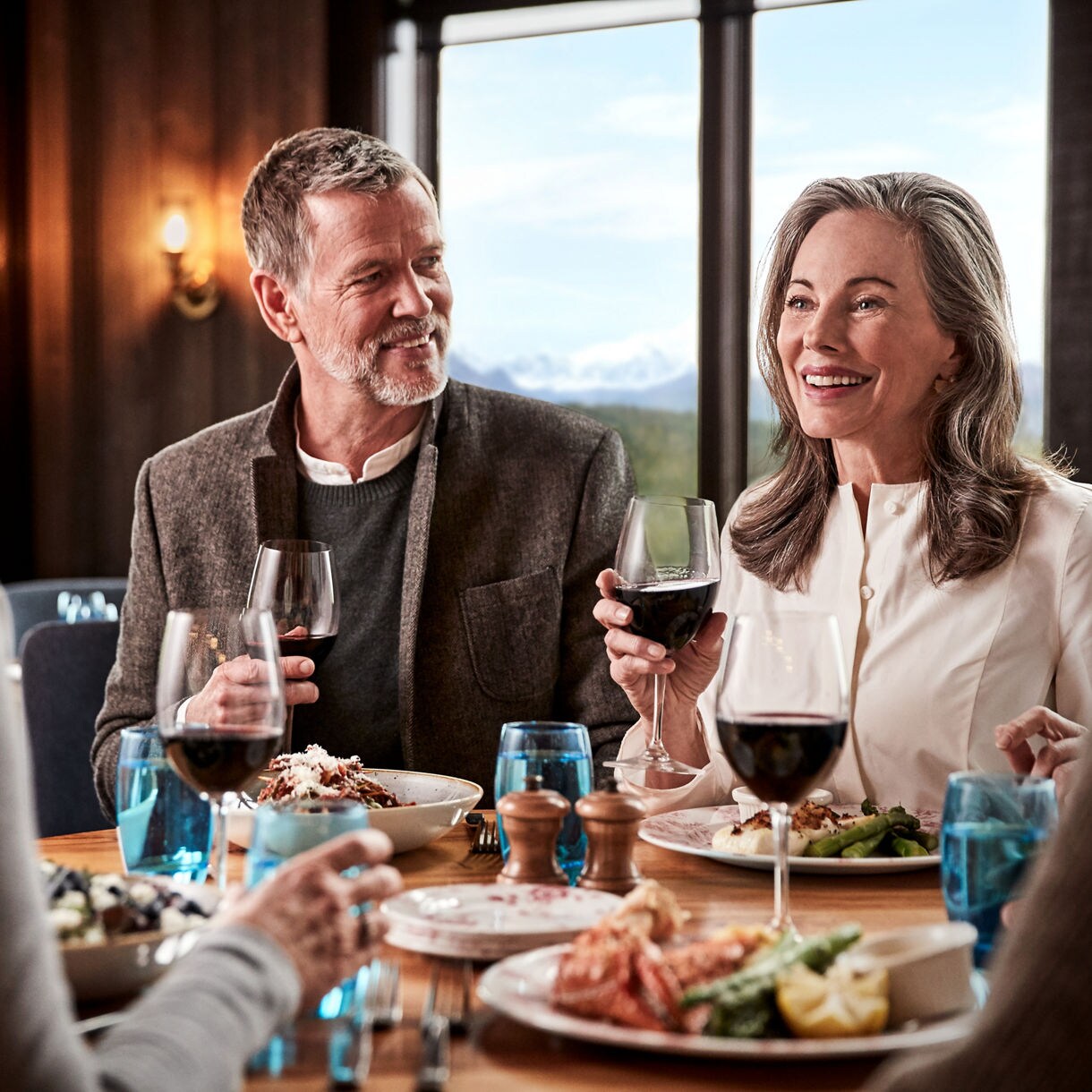 A plated dish of creamy pasta topped with shrimp and garnished with herbs, served on a white plate atop a patterned tablecloth with a glass of wine nearby.