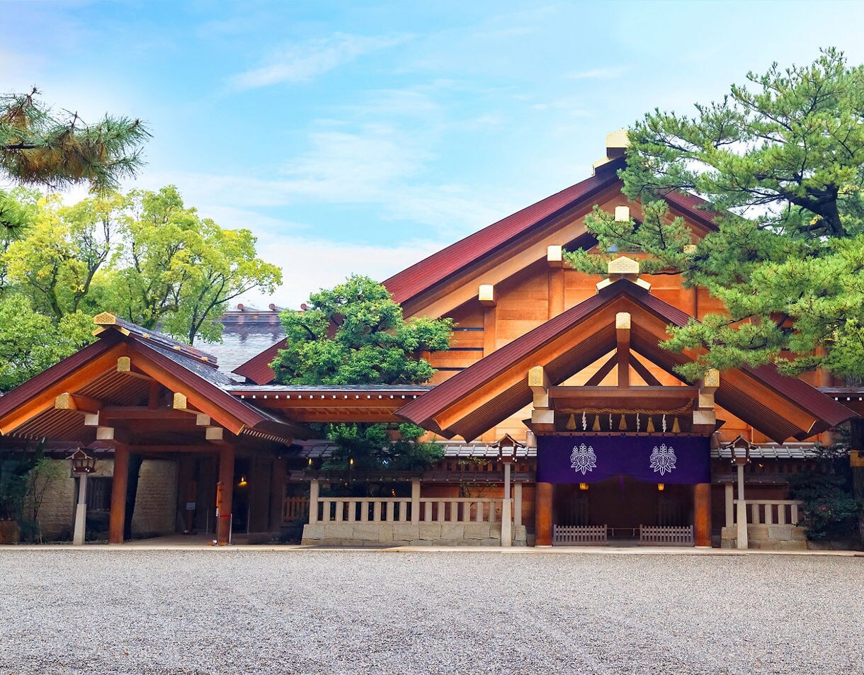 Front view of Atsuta Shrine in Nagoya, showcasing its wooden architecture framed by lush green trees under a bright sky.