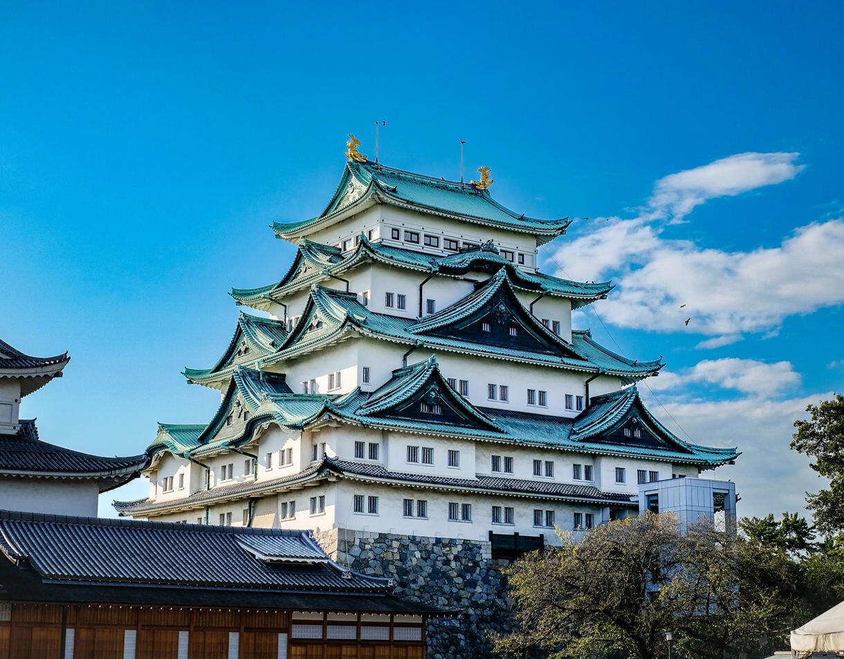 Nagoya Castle with tiered green-tiled roofs and golden ornaments under a bright blue sky.