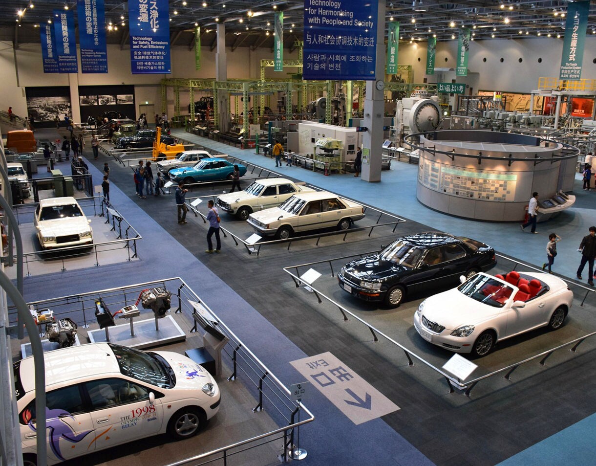 Exhibit hall at the Toyota Commemorative Museum in Nagoya, displaying classic cars, engines and visitors walking among the showcases.
