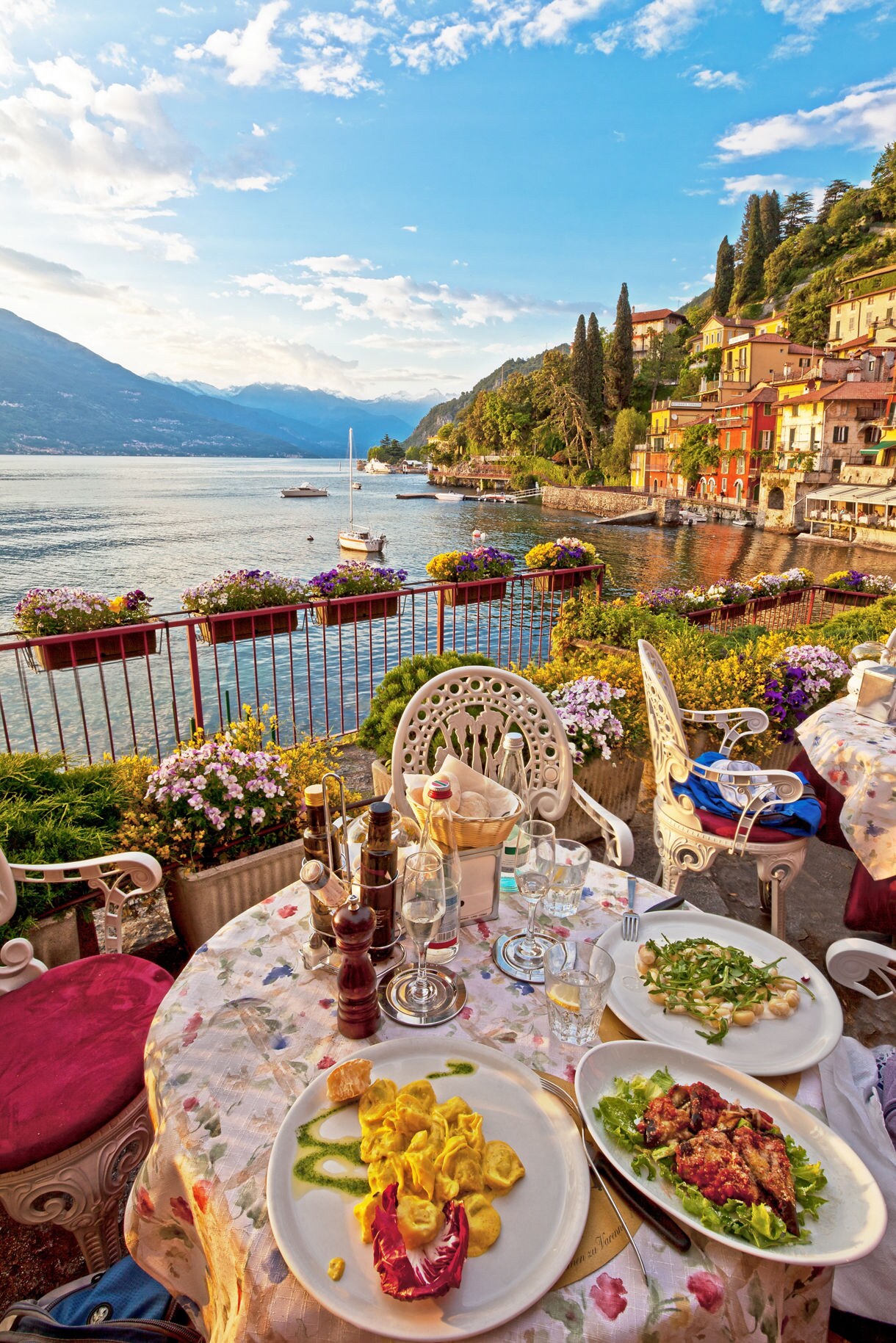 Outdoor table set with pasta and Italian dishes overlooking Lake Como and colorful lakeside houses.