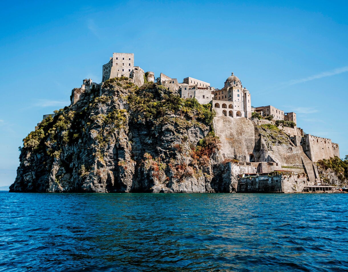 Stone fortress of Castello Aragonese perched on a rocky cliff over the sea on Ischia island, Italy.