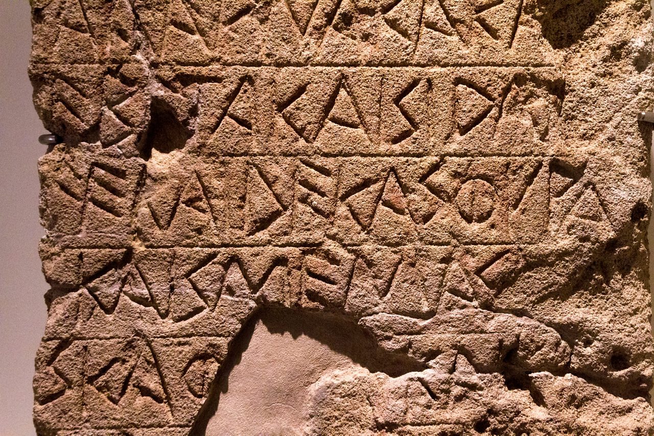 Close-up of an ancient stone slab with carved geometric inscriptions on display at the Naples Archaeological Museum.