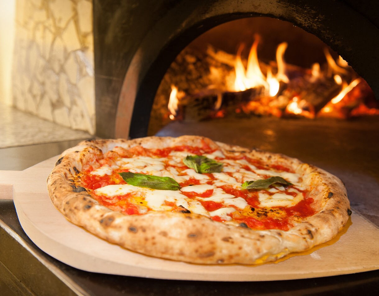 Traditional Neapolitan pizza topped with mozzarella, tomato sauce and basil baking in a wood-fired oven.