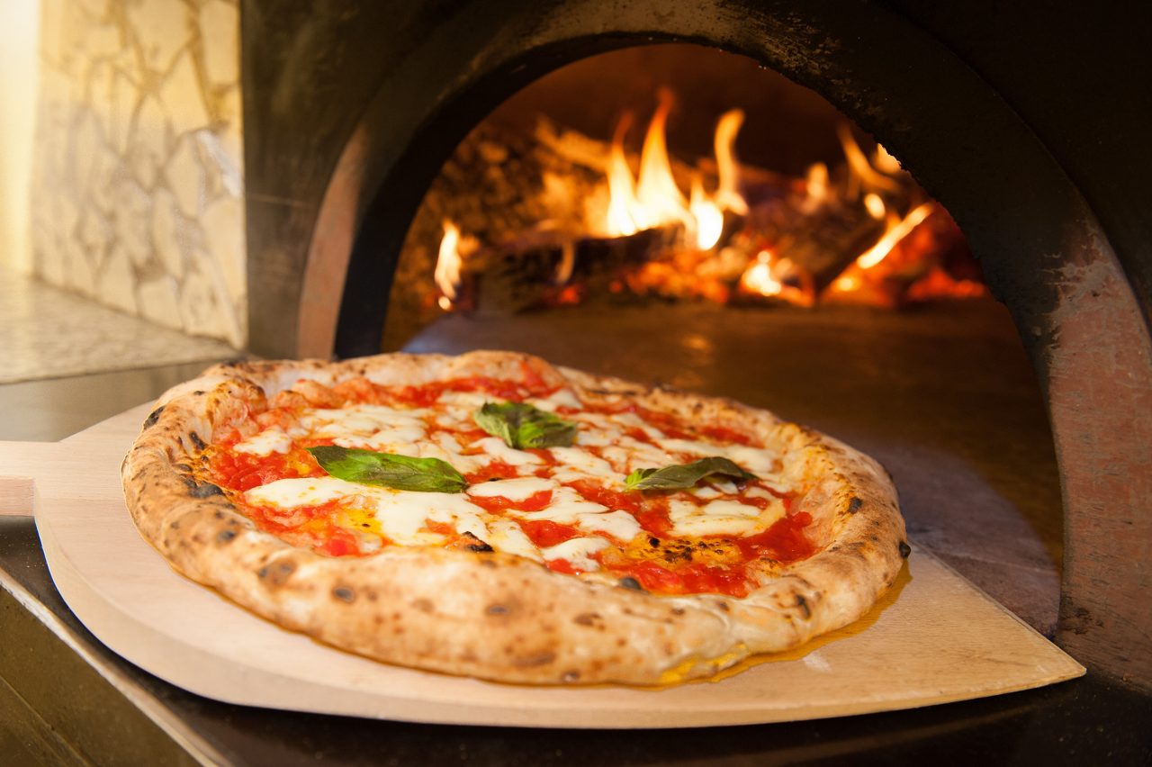 Classic Neapolitan pizza with melted mozzarella, tomato sauce, and basil leaves baking in a wood-fired oven.