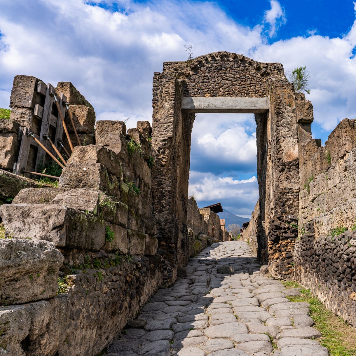 Preserved stone archway and cobbled street in the ruins of Pompeii, surrounded by weathered walls and greenery.