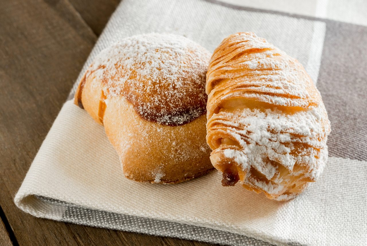 Two sfogliatelle pastries on a folded napkin, golden and dusted with powdered sugar.