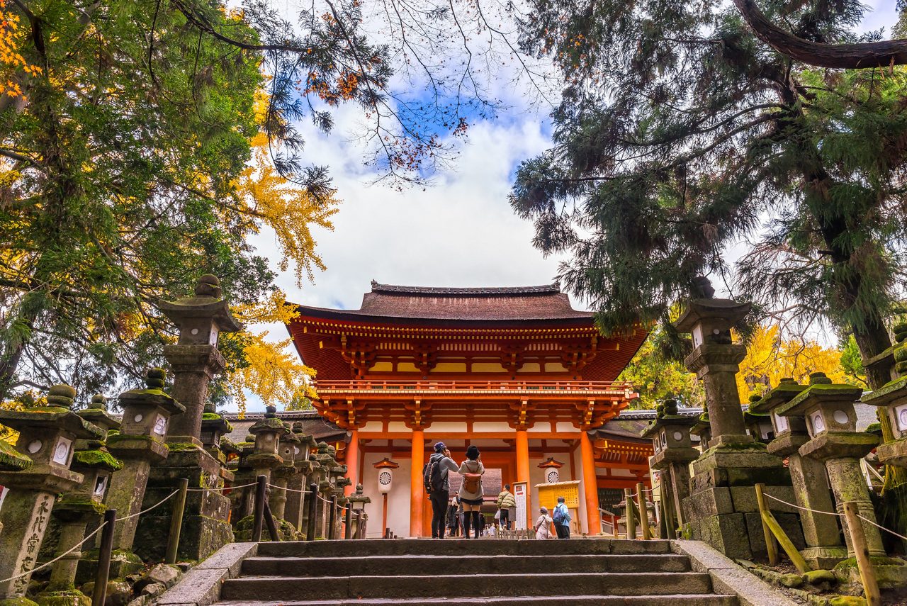 Alt text: A stunning view of Kinkakuji Temple, the Golden Pavilion, in Kyoto, Japan, with its golden exterior reflecting on the calm waters of a pond, surrounded by trees and colorful foliage on a sunny day. 