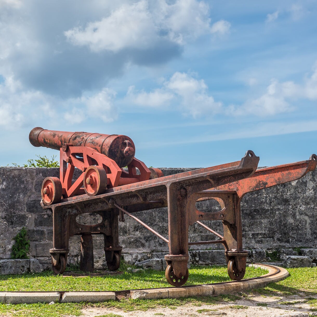 Historic red cannon positioned on stone fortification walls with ocean view under partly cloudy sky at Nassau fort.