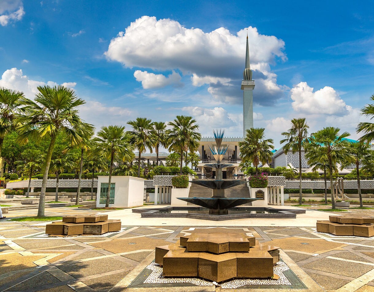 The National Mosque of Malaysia in Kuala Lumpur featuring a tall minaret, geometric fountain and palm-lined courtyard.