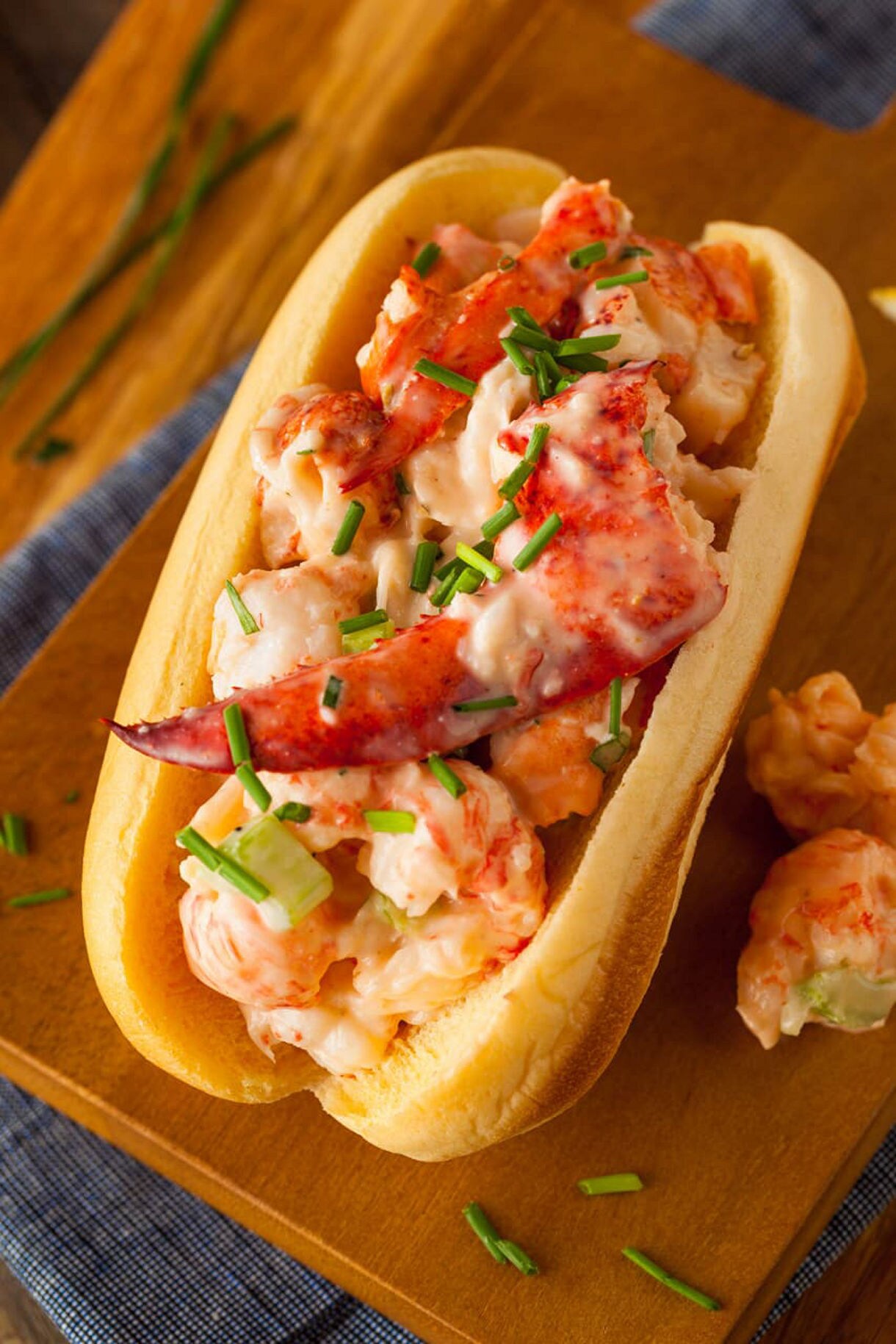 Close-up of a lobster roll filled with creamy lobster chunks and garnished with chopped chives in a toasted bun.