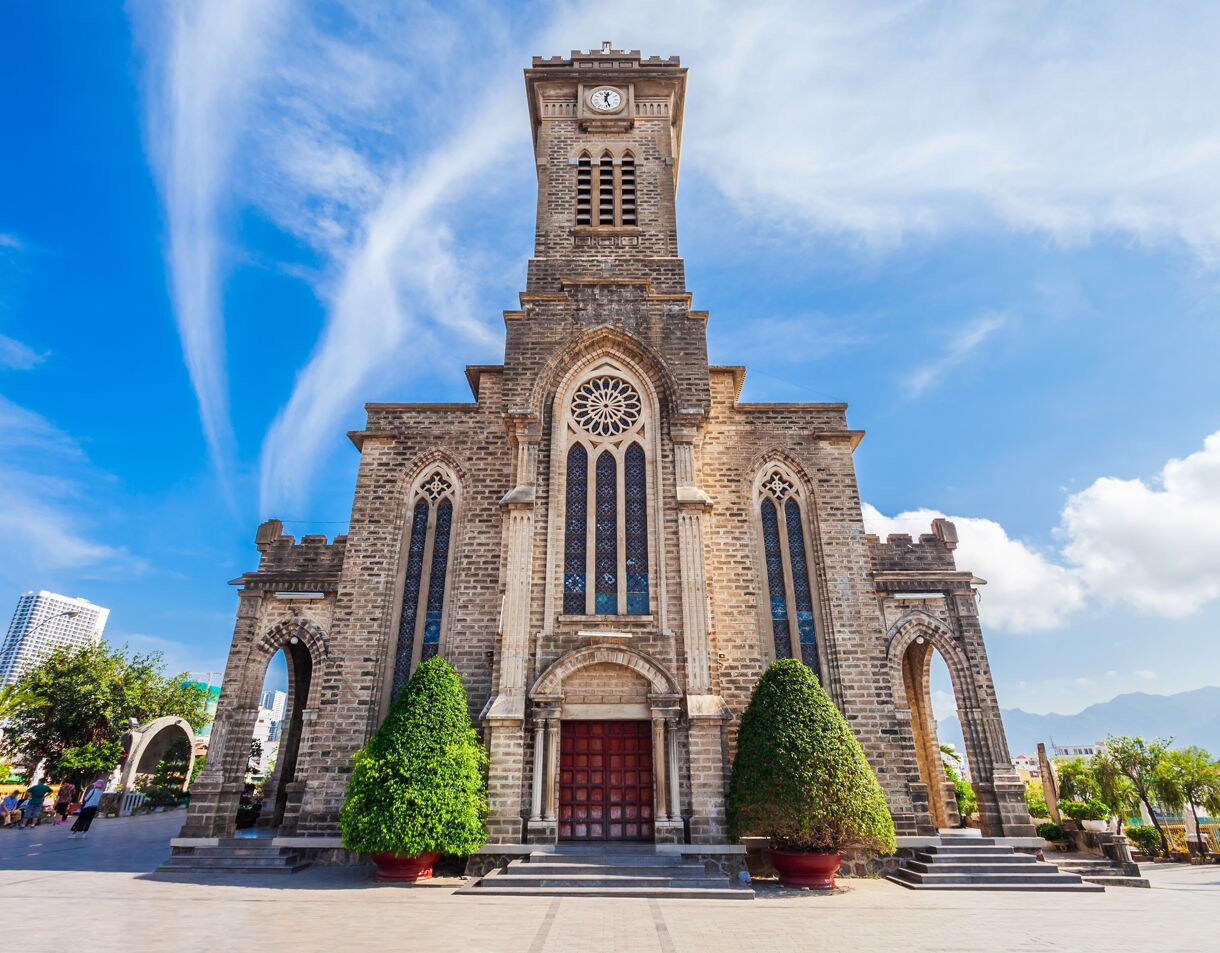 Front view of Nha Trang Cathedral in Vietnam, showcasing its Gothic-style stone architecture and stained glass windows under a vivid blue sky.